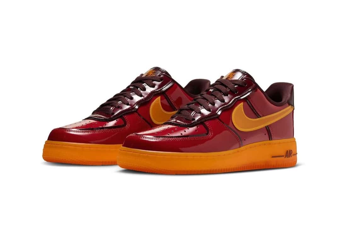 Par de Nike Air Force 1 Iron Man visto de tres cuartos, con el charol rojo brillante, los cordones bordó y la suela naranja