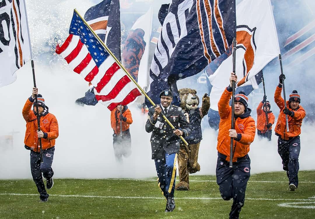 Foto de archivo: un soldado con la bandera de Estados Unidos y abanderados de los Chicago Bears, de naranja, entran corriendo a la cancha del Soldier Field entre humo y nieve antes de un partido