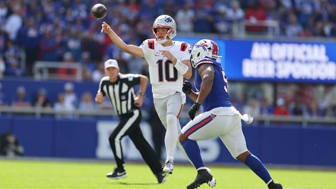 Drake Maye, con la camiseta blanca número 10 de los Patriots, lanza un pase mientras un defensor de los Bills lo persigue