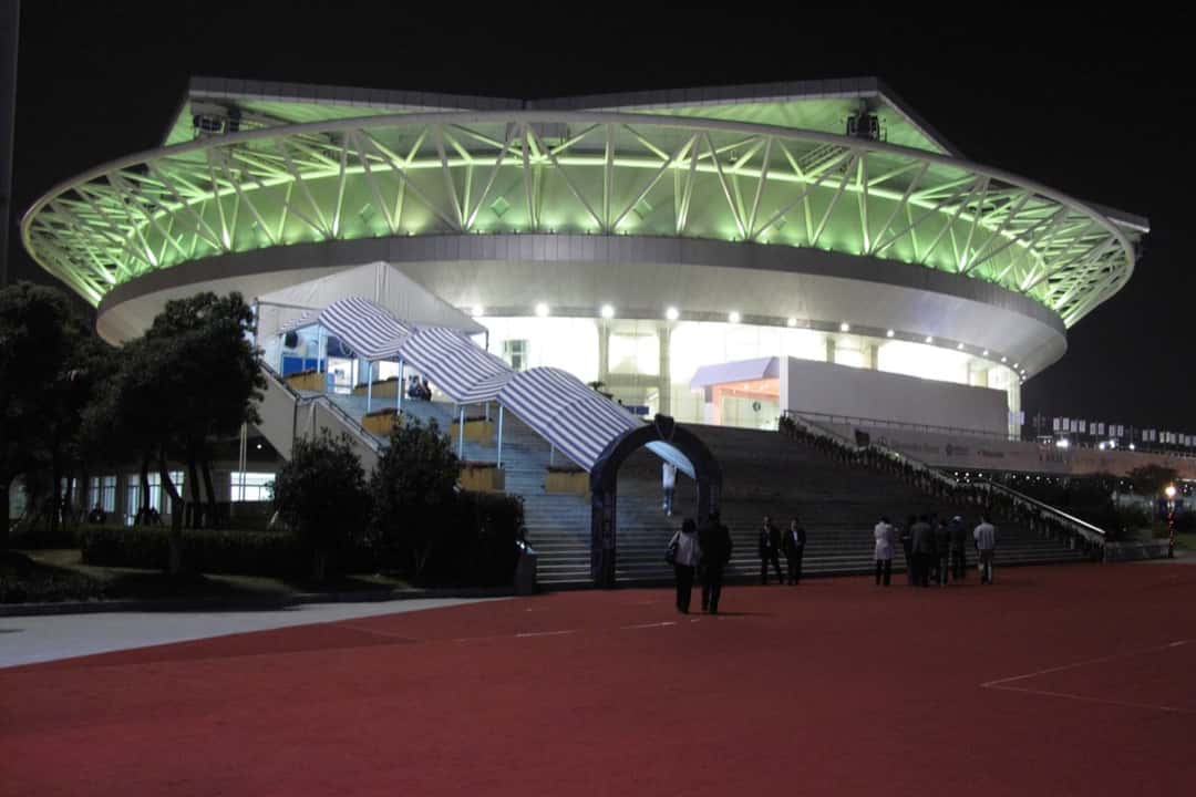 Foto de archivo: el Qi Zhong Stadium de Shanghái de noche, con la estructura del techo iluminada en verde y la escalinata de acceso