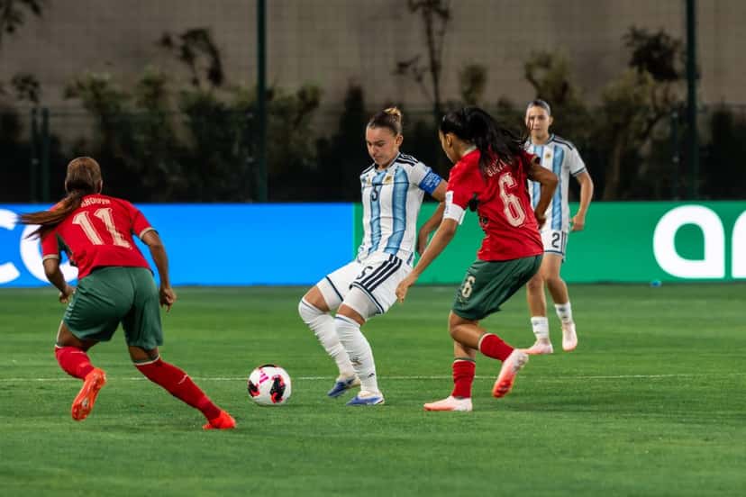 Una jugadora argentina, con la camiseta celeste y blanca, maneja la pelota entre dos rivales de Marruecos, de camiseta roja, en el partido del Mundial Sub-17 (foto: prensa oficial de la AFA)
