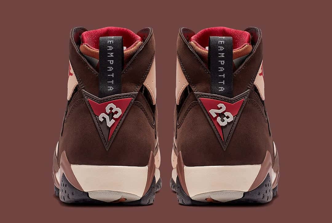 Foto de archivo: vista trasera del par de Patta x Air Jordan 7 Shimmer de 2019, con el tirador negro que dice TEAMPATTA, el triángulo rojo con el número 23 y la suela en tonos crema y gris