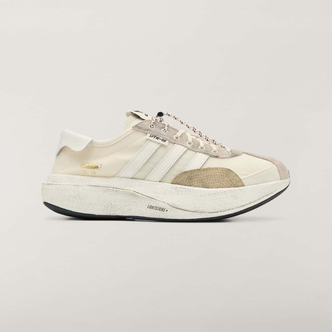 Vista lateral del adidas SL 72 PRO Cream White de Song for the Mute, con capellado textil crema, tres tiras blancas dentadas, refuerzos de gamuza beige con aspecto gastado, cordón jaspeado con toggle, etiqueta SFTM-011 y mediasuela blanca envejecida con la inscripción Lightstrike+