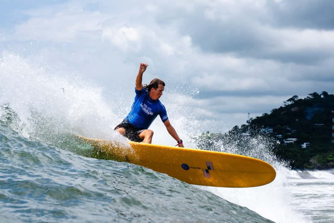 Tony Silvagni, con lycra azul, hace un giro fuerte sobre un longboard amarillo frente a la costa verde de El Sunzal