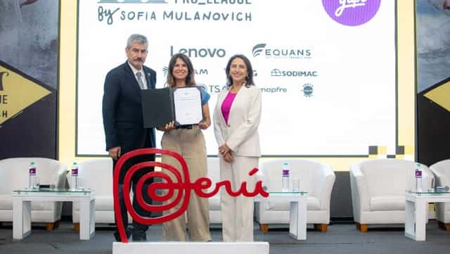 Sofía Mulanovich sostiene una carpeta con la licencia de la Marca Perú entre un hombre de traje y una mujer de blanco, detrás del logo rojo de la marca país y frente a una pantalla del Surf Fest Pro League
