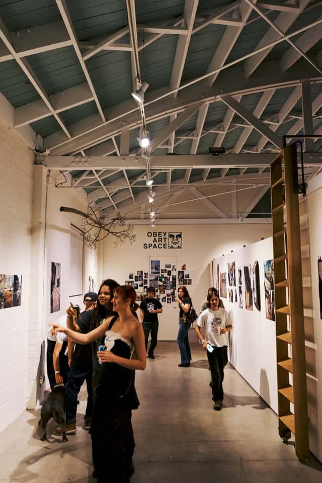 Gente recorre la galería del OBEY Art Space de Los Ángeles, con fotos de skate colgadas en las paredes blancas y el logo de la marca al fondo