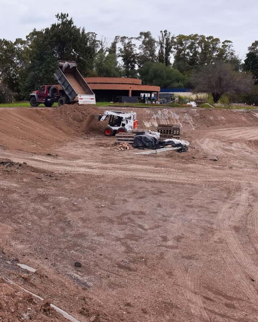 Obras en la vieja pista de BMX del Parque Sarmiento: un camión volcador descarga tierra y una minicargadora mueve el suelo frente al anfiteatro de ladrillo, en mayo de 2026
