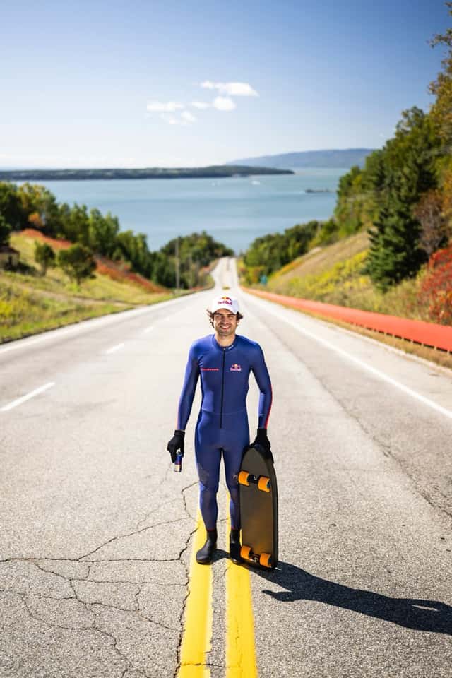 Diego Poncelet, con traje azul y gorra blanca, posa en el medio de la ruta con su skate en la mano y el río San Lorenzo de fondo