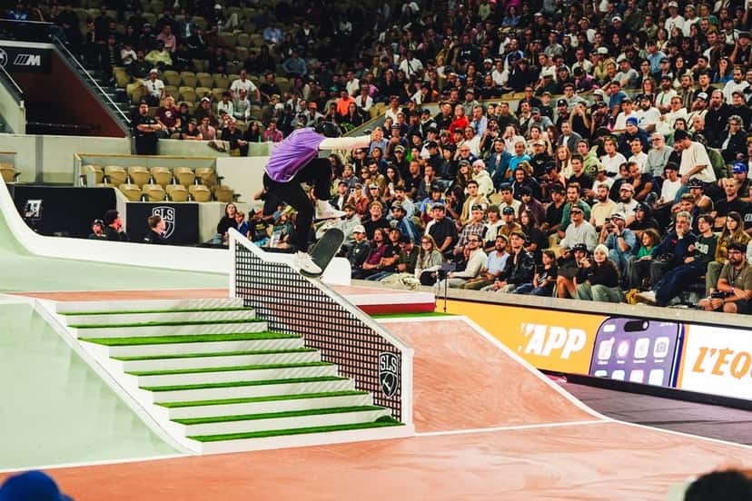 Nyjah Huston, con remera violeta, desliza la tabla sobre la baranda de la escalera del parque armado en Roland-Garros, con la tribuna llena detrás