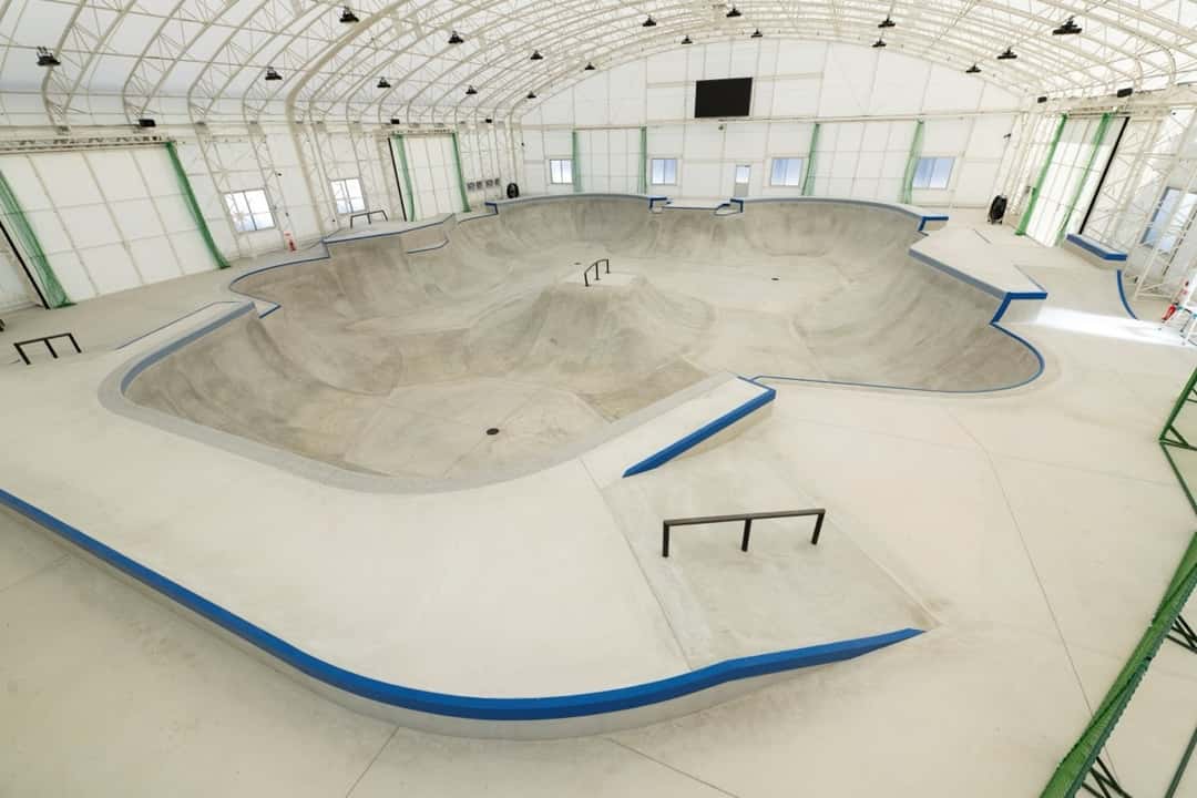 El bowl de hormigón del Tenjin Street Park, con bordes azules, barandas y una pirámide en el centro, bajo el techo de arcos blancos