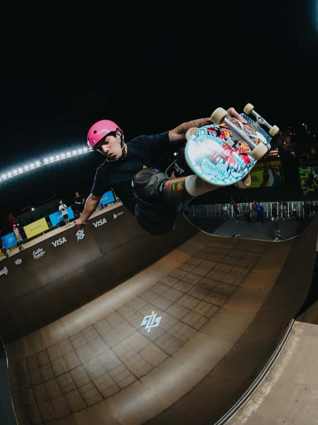 Un skater con casco rosa agarra la tabla en el aire por encima del borde de una rampa vertical, de noche, en una fecha anterior del Vert Battle (foto de archivo)