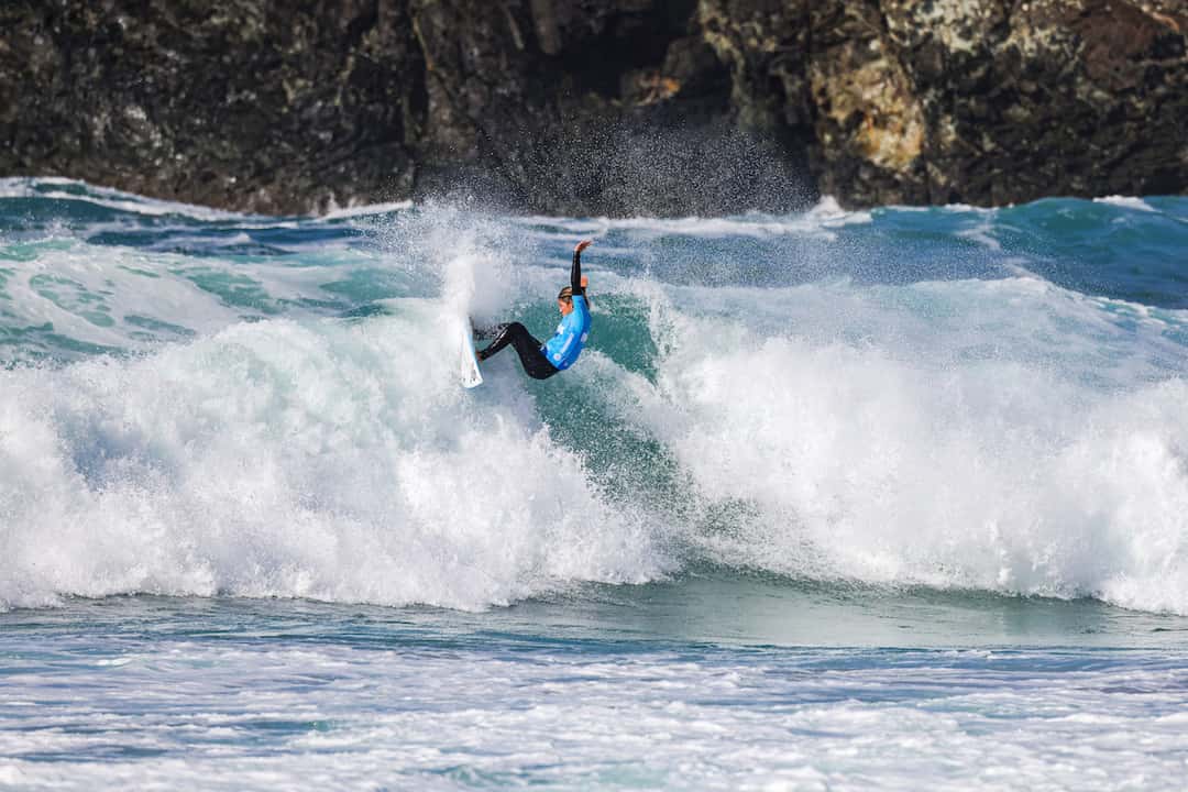Catalina Zariquiey, con lycra celeste, gira en la cresta de una ola con espuma blanca, frente a unas rocas, en una fecha del circuito de clasificación de la WSL (foto de archivo)