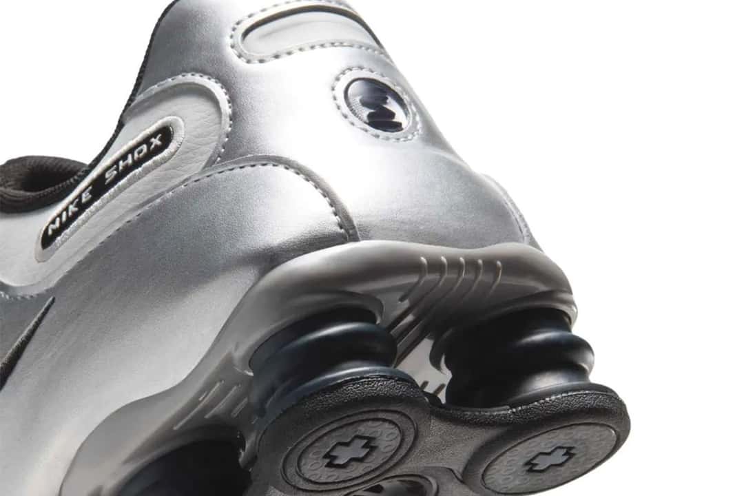Talón de la Nike Shox NZ Photon Dust/Metallic Silver, con el logo circular de Shox, la inscripción Nike Shox y las columnas de amortiguación