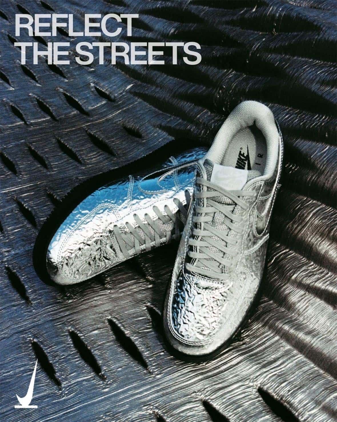 Par de Nike Air Force 1 '01 Chrome con el upper plateado arrugado y reflectivo y la suela negra, apoyado sobre una superficie oscura texturada, en la imagen oficial de SNKRS con la frase Reflect the Streets
