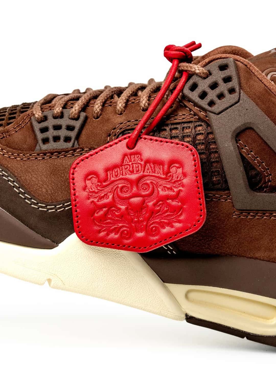 Detalle del Air Jordan 4 BIN 23 con el colgante de cuero rojo grabado y las rejillas laterales