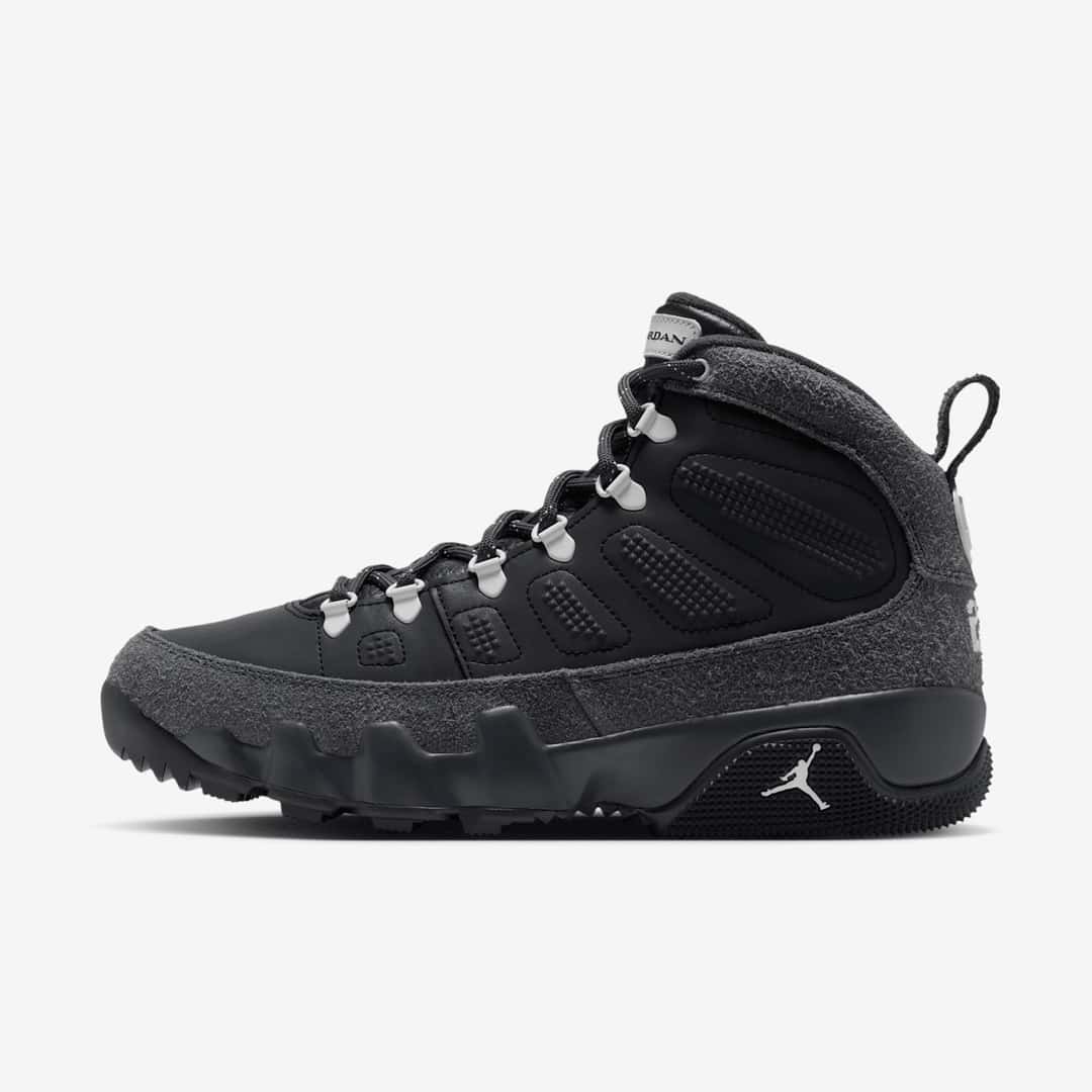Air Jordan 9 Retro Boot NRG Anthracite de perfil sobre fondo blanco, con el cuerpo de cuero negro y sus relieves, gamuza gris oscura en la base, el cuello y el talón, ojales de metal con terminales grises, tira para calzarse en el talón y suela negra con el Jumpman blanco