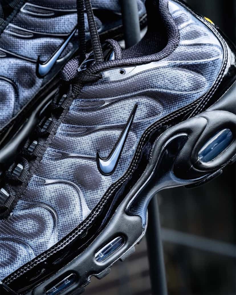 Detalle del costado del Nike Air Max Plus negro y gris con el patrón de puntos sobre la malla, las ondas laterales con el mismo efecto, el Swoosh y la burbuja de aire