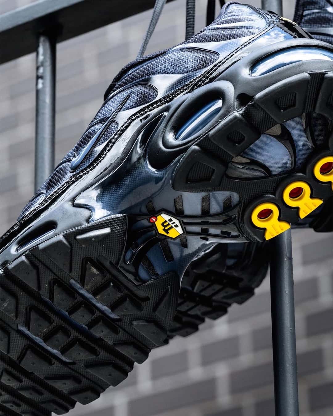 Suela del Nike Air Max Plus negro y gris vista en diagonal, con la goma negra, las piezas amarillas del arco y las burbujas de aire azuladas en la mediasuela
