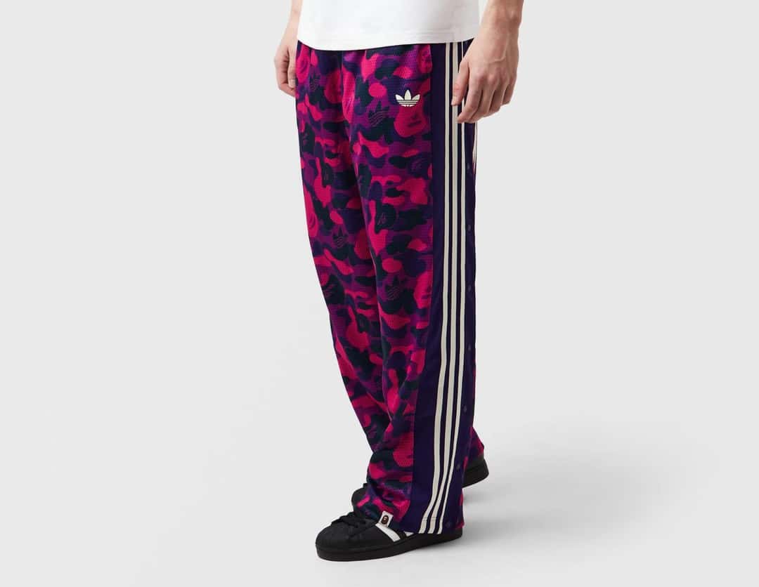 Modelo con el pantalón deportivo BAPE x adidas de camuflaje rosa y violeta con las tres tiras blancas a los costados