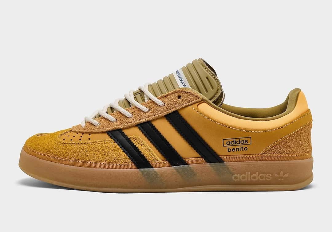 Vista lateral de la Bad Bunny x adidas Gazelle Indoor Solar Gold con branding adidas benito en el talón, tres tiras negras y suela gum translúcida