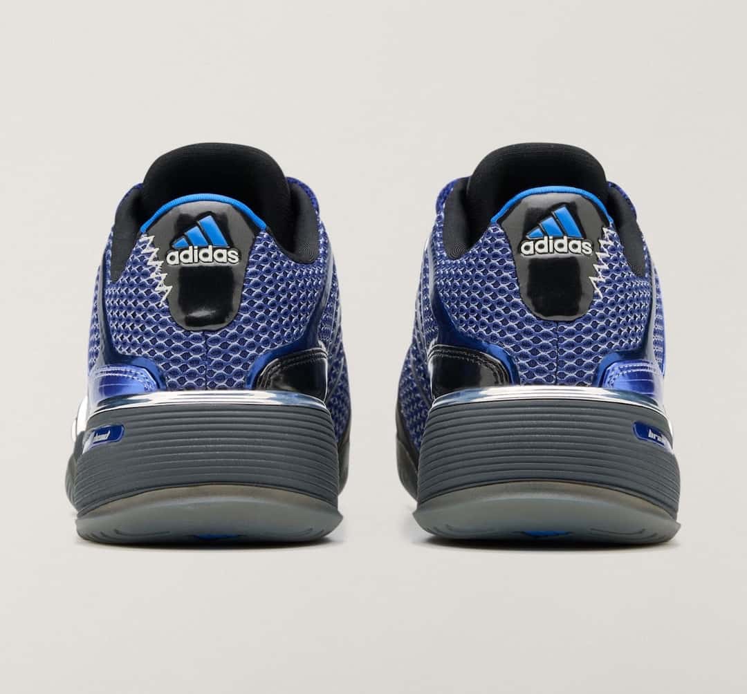 Vista trasera del par del Brain Dead x adidas Barricade V Mystery Ink sobre fondo gris claro, con malla azul, talón negro con el logo de adidas en azul y blanco, detalles azules brillantes y suela gris oscura con base translúcida