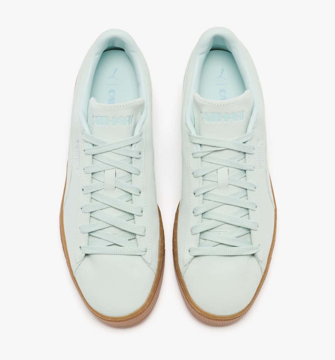 Vista superior del par PUMA Suede Sea Glass de Daniëlle Cathari, con la marca Cathari grabada en la lengüeta, cordones planos verde agua y plantilla celeste con los logos de PUMA y Cathari