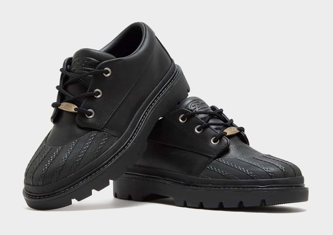 Par del Converse 1908 Bronco Boot Low negro, todo en cuero negro con puntera de goma texturada, ojales plateados, plaqueta dorada en los cordones y suela dentada negra