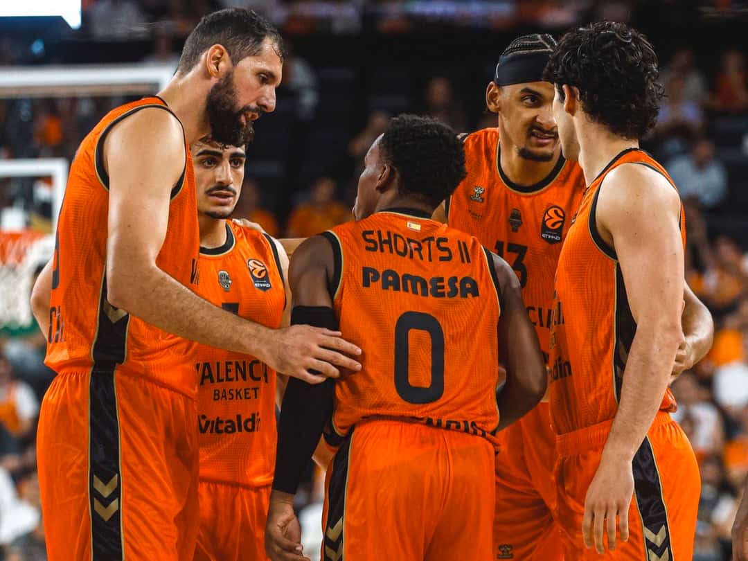 TJ Shorts, de espaldas con la camiseta naranja número 0, y sus compañeros del Valencia Basket conversan en ronda durante un partido de Euroliga en el Roig Arena