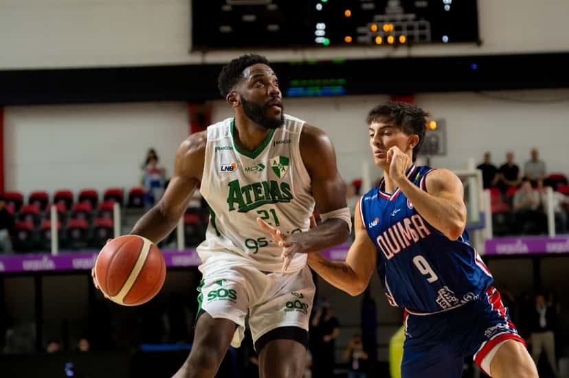 Un jugador de Atenas con la camiseta blanca 21 avanza con la pelota ante la marca de un jugador de Quimsa con la camiseta azul 9