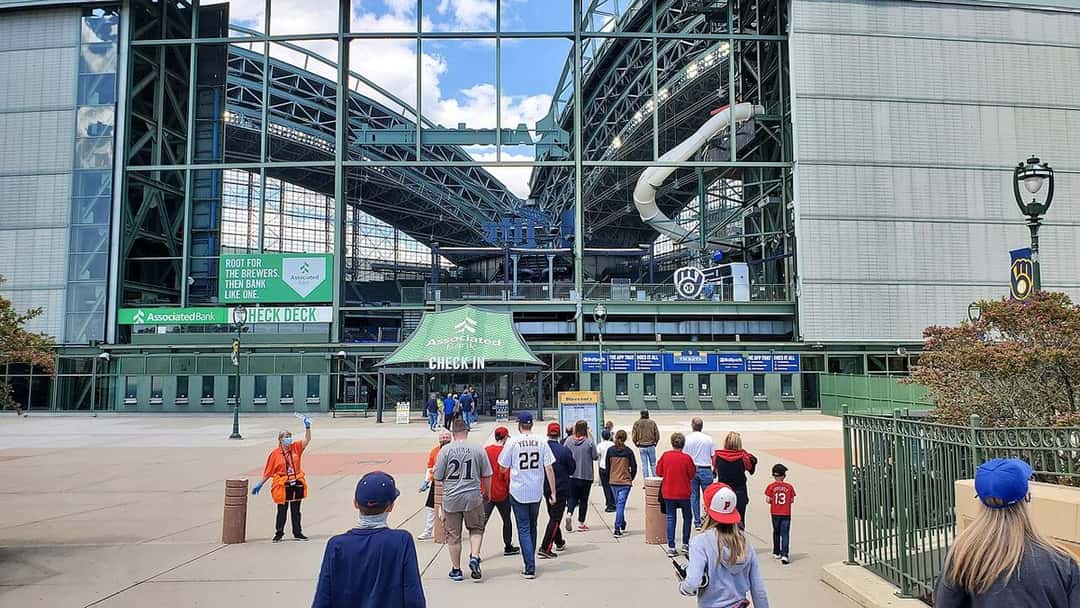 Imagen del estadio: hinchas de los Brewers caminan hacia la entrada del American Family Field de Milwaukee, con el techo retráctil abierto
