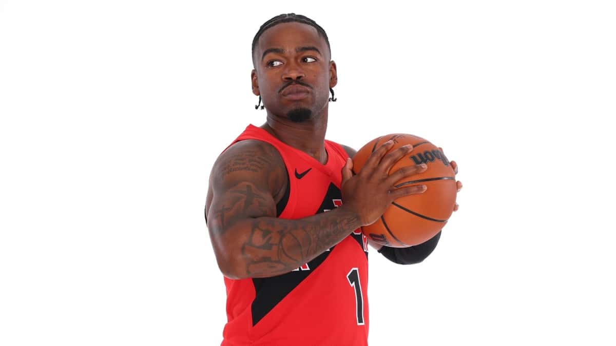 Jamal Shead con la camiseta roja de los Toronto Raptors sostiene una pelota en una sesión de fotos sobre fondo blanco