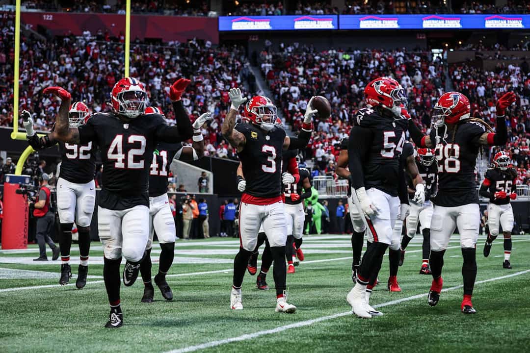 Los defensores de los Falcons, con camisetas negras, festejan con los brazos en alto una intercepción de Jessie Bates III en el campo del Mercedes-Benz Stadium