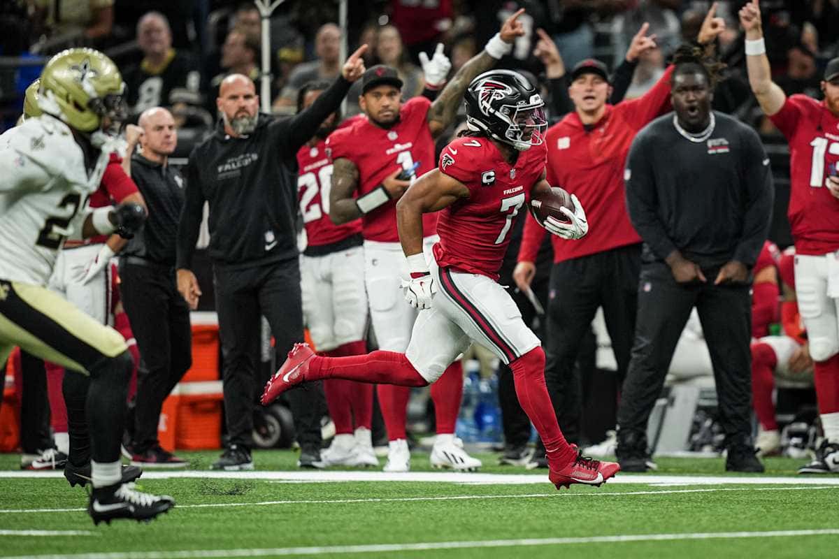 Bijan Robinson, con la camiseta roja número 7 de los Falcons, corre con la pelota por la banda mientras sus compañeros festejan detrás en el Caesars Superdome