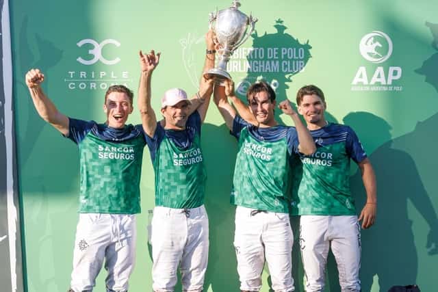 Los cuatro jugadores de La Natividad La Dolfina, con camisetas verdes, festejan en el podio con los brazos en alto mientras levantan la copa del Abierto de Hurlingham