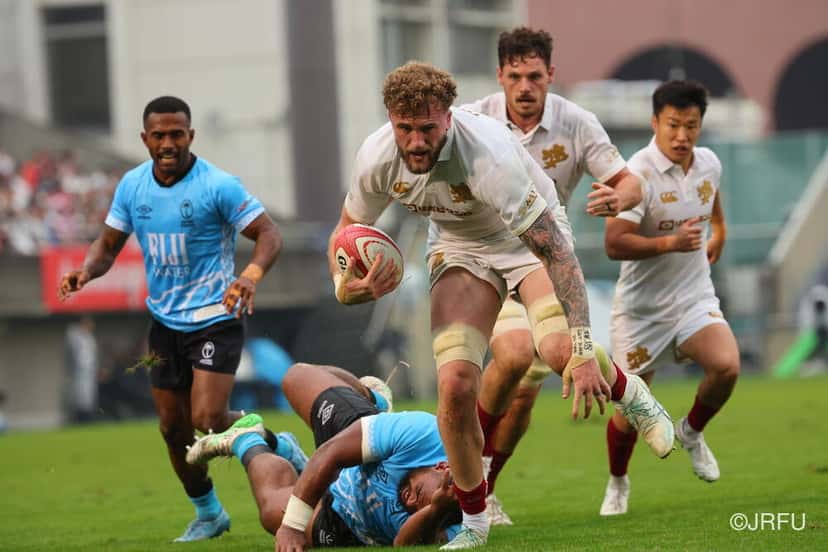Un forward de Japón, de blanco, corre con la pelota entre jugadores de Fiyi caídos, en el test del sábado 24 en Tokio