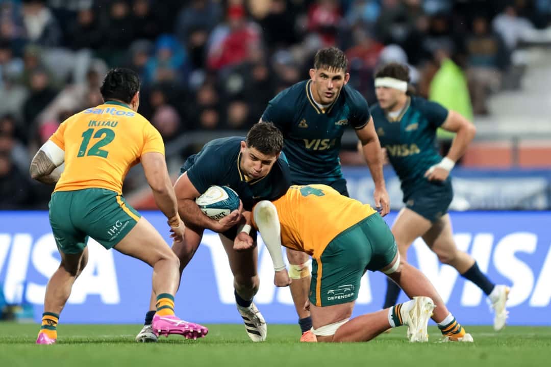 Un jugador de Los Pumas, con la camiseta azul oscuro, avanza con la pelota entre dos rivales de Australia, de camiseta amarilla, en el estadio Malvinas Argentinas de Mendoza