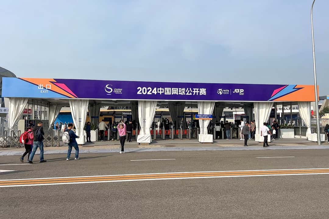 La entrada sur del Centro Nacional de Tenis de Beijing durante el China Open 2024, con el cartel del torneo y gente ingresando