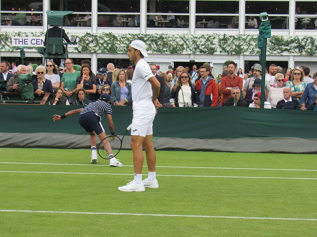 Foto de archivo: Francisco Cerúndolo, de blanco y con gorra, camina por una cancha de césped en Wimbledon con el público detrás