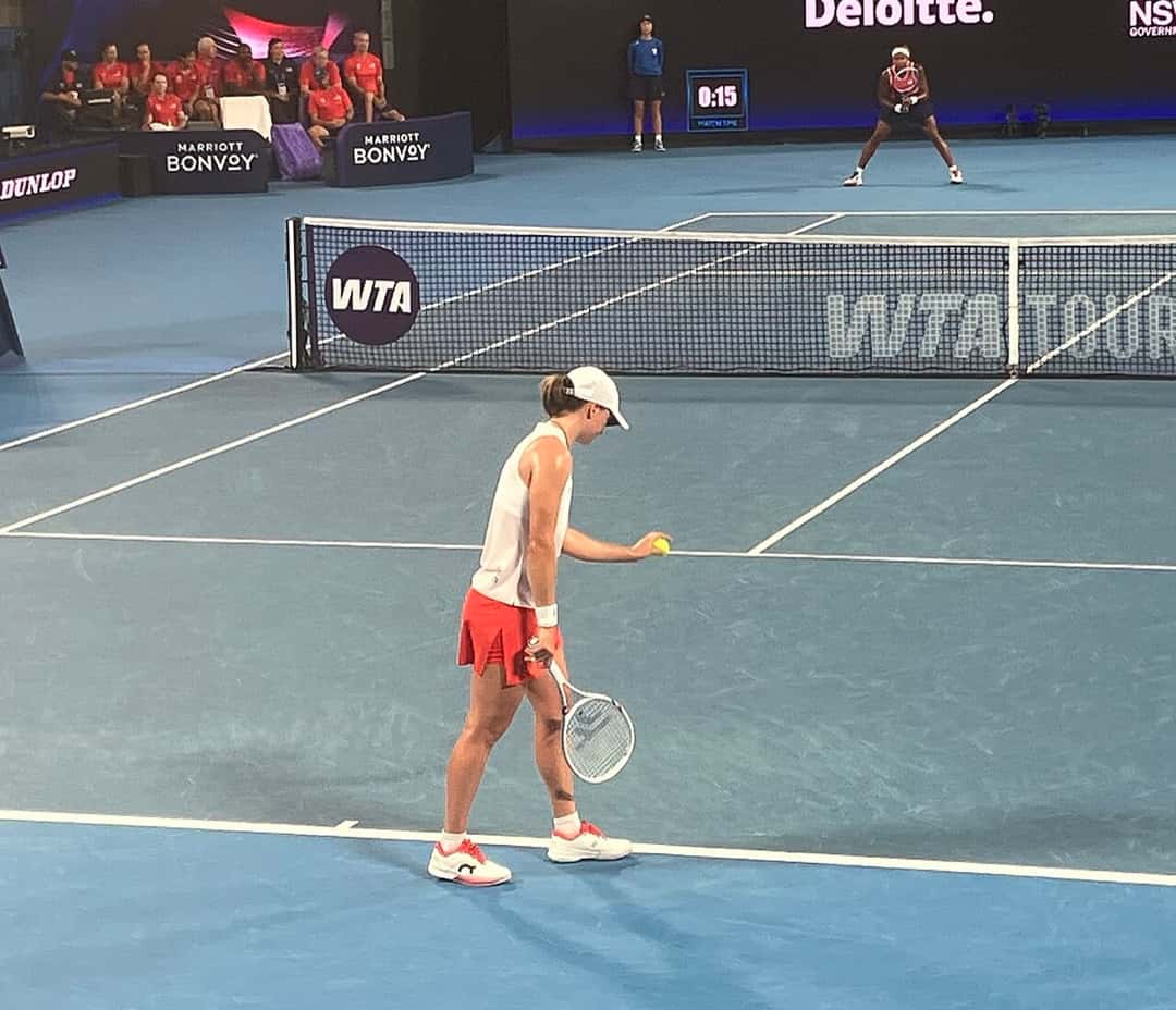 Foto de archivo: Iga Swiatek, con gorra blanca, remera blanca y pollera roja, se prepara para sacar en la semifinal de la United Cup 2026, con Coco Gauff al fondo