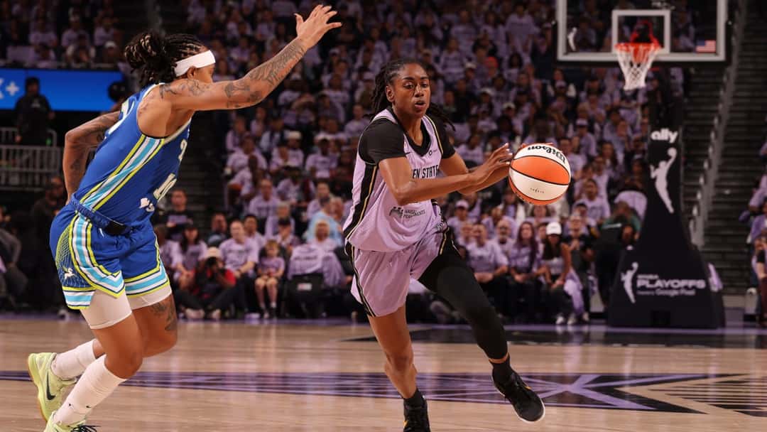 Una jugadora de Golden State Valkyries ataca con la pelota ante la marca de una jugadora de Dallas Wings, con el estadio lleno de hinchas vestidos de violeta