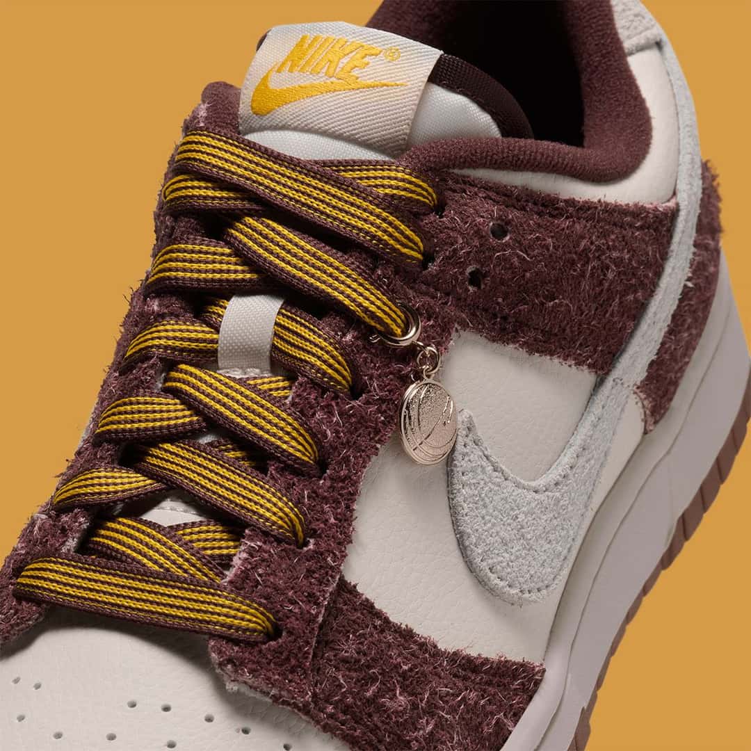 Detalle de la Nike Dunk Low Basketball Charm, con los cordones bordó y dorado, el dije metálico de pelota de básquet y la gamuza peluda bordó