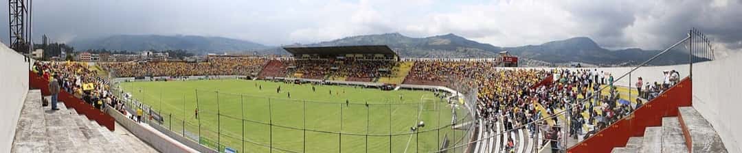 Vista panorámica del estadio Gonzalo Pozo Ripalda, de Aucas, en Quito, con hinchas en las tribunas durante un partido y las montañas de fondo; foto de archivo de noviembre de 2014 (foto: ground.hopper, Wikimedia Commons, licencia CC BY-SA 2.0)