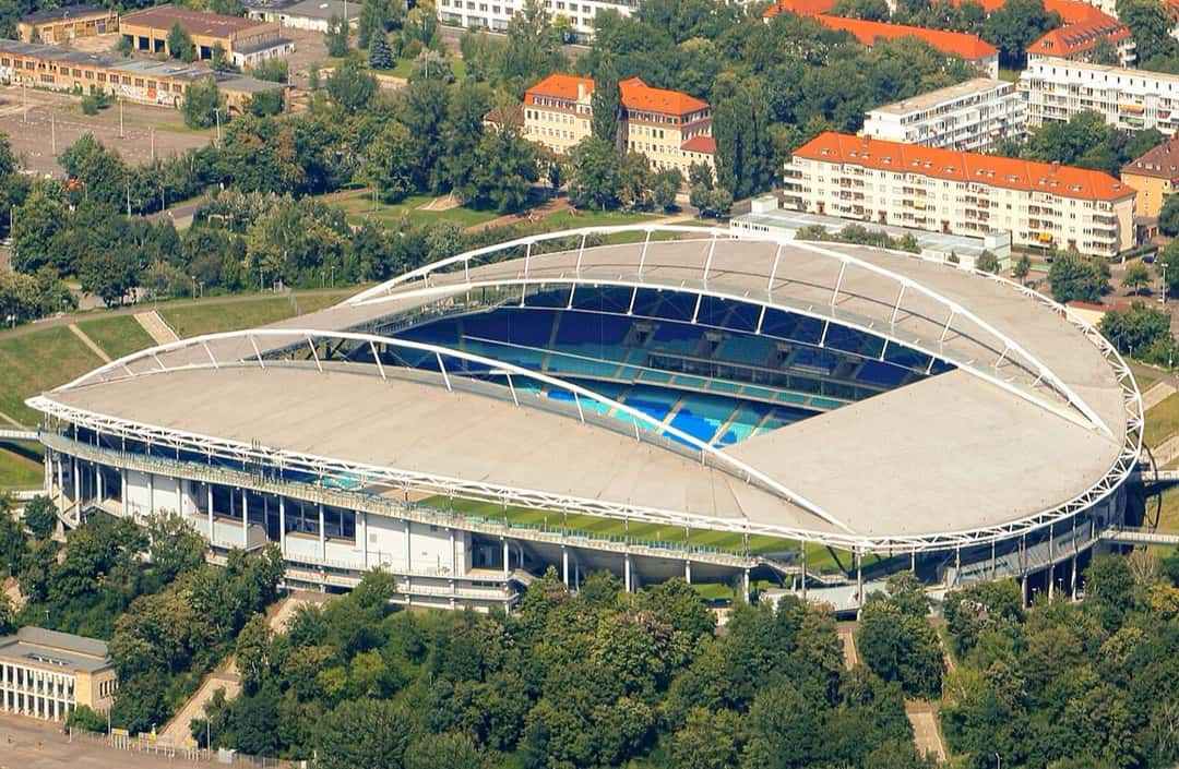 La Red Bull Arena de Leipzig vista desde el aire, con el techo y las tribunas azules, rodeada de árboles; foto de archivo de julio de 2011 (foto: Philipp, Wikimedia Commons, licencia CC BY 2.0)