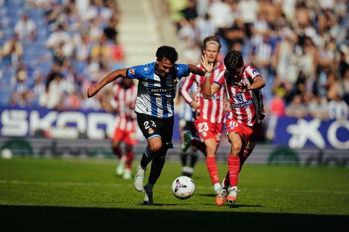 Un jugador del Espanyol, con la camiseta blanca y azul, protege la pelota ante dos futbolistas del Atlético de Madrid, de rojo y blanco, en el RCDE Stadium (foto: prensa RCD Espanyol)