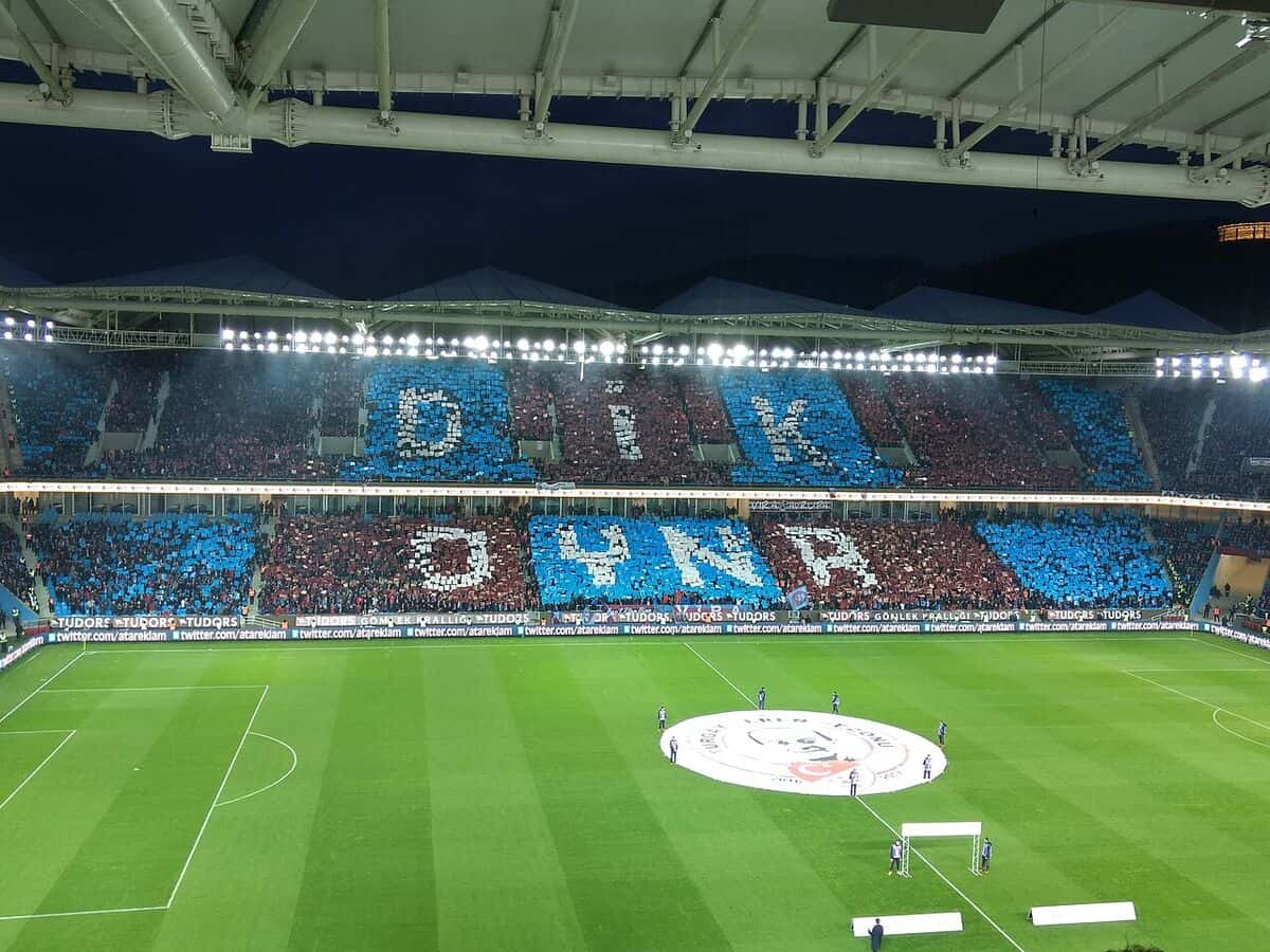 Las tribunas del estadio del Trabzonspor, en Trabzon, cubiertas con un mosaico bordó y celeste antes de un partido, con la cancha iluminada; foto de archivo de 2017 (foto: Myrat, Wikimedia Commons, licencia CC BY-SA 4.0)
