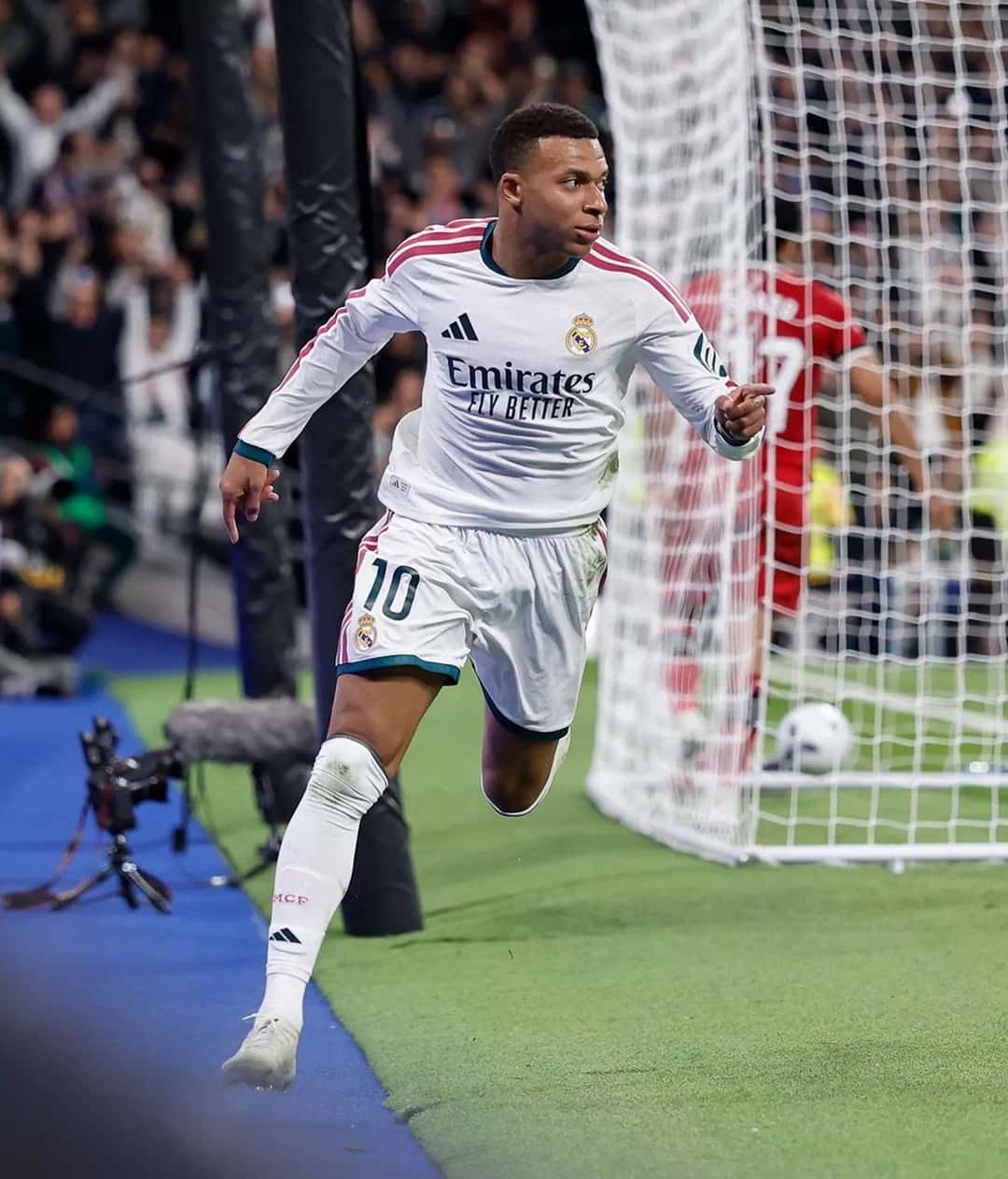 Kylian Mbappé, con la camiseta blanca del Real Madrid y el número 10, corre a festejar uno de sus goles junto al arco, con el Bernabéu de fondo (foto: Real Madrid C.F.)
