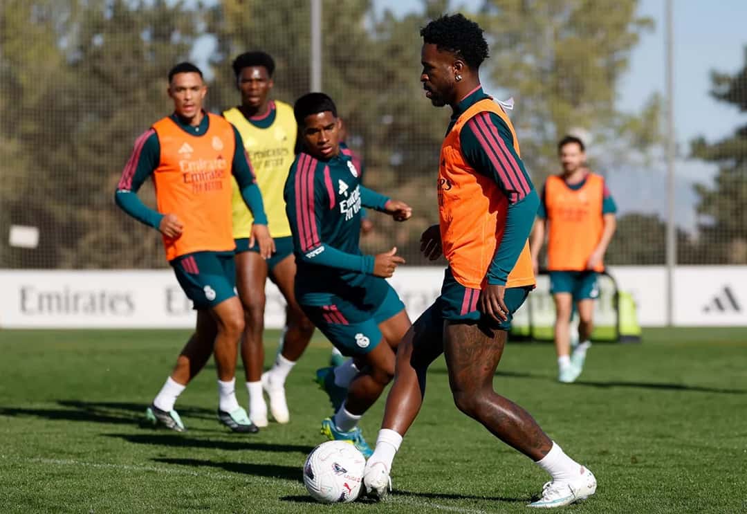 Vinícius Júnior maneja la pelota en el último entrenamiento antes del partido con el Villarreal, observado por compañeros con pecheras de colores en la Ciudad Real Madrid (foto: Real Madrid C.F.)