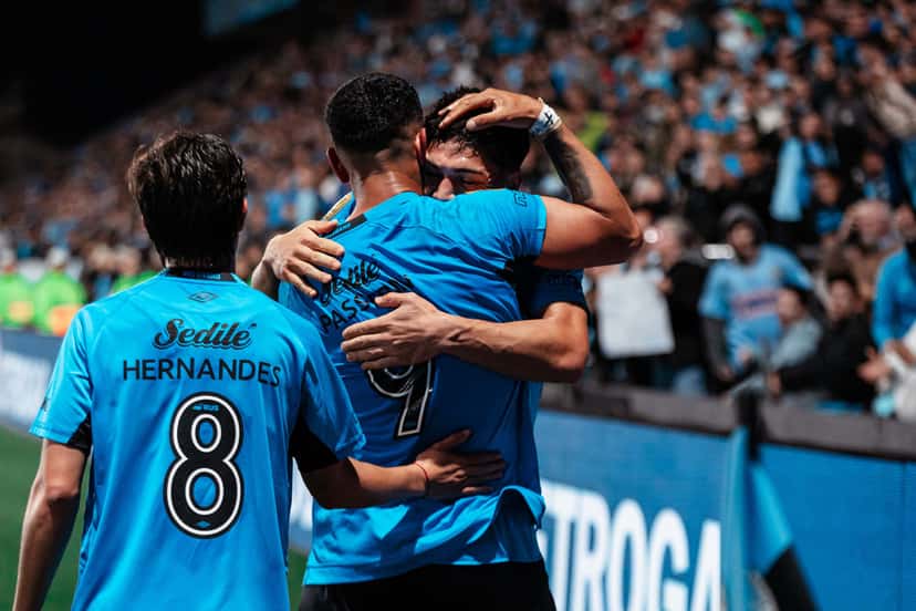 Jugadores de Belgrano se abrazan para festejar un gol ante Estudiantes de Río Cuarto