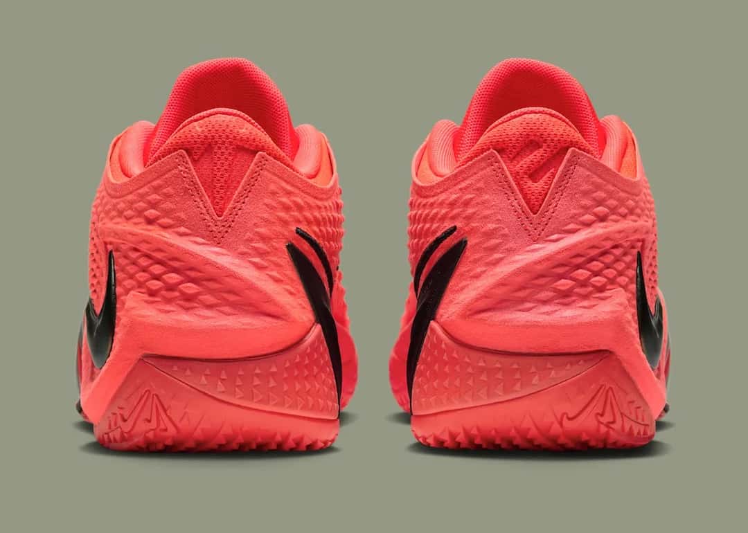 Talones de la Nike Ja 4 Code Red, rojos con la pieza oscura que baja por el costado, sobre fondo verde grisáceo