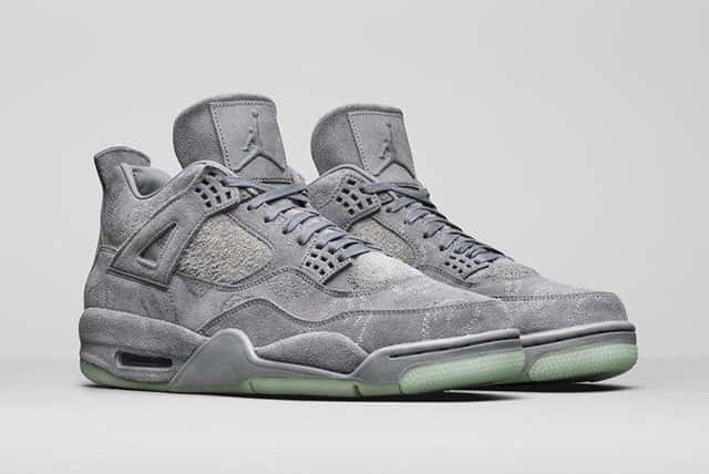 Foto de archivo: KAWS x Air Jordan 4 Cool Grey de 2017 en foto oficial de producto, vista de tres cuartos sobre fondo gris claro, con gamuza gris, bordados de las manos de KAWS en el upper y suela translúcida verde agua